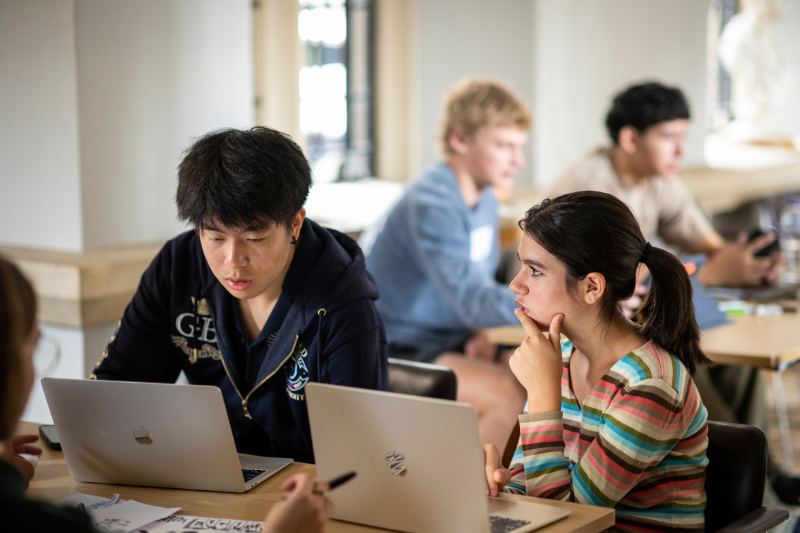 Student stands at the front of a classroom near a whiteboard and podium