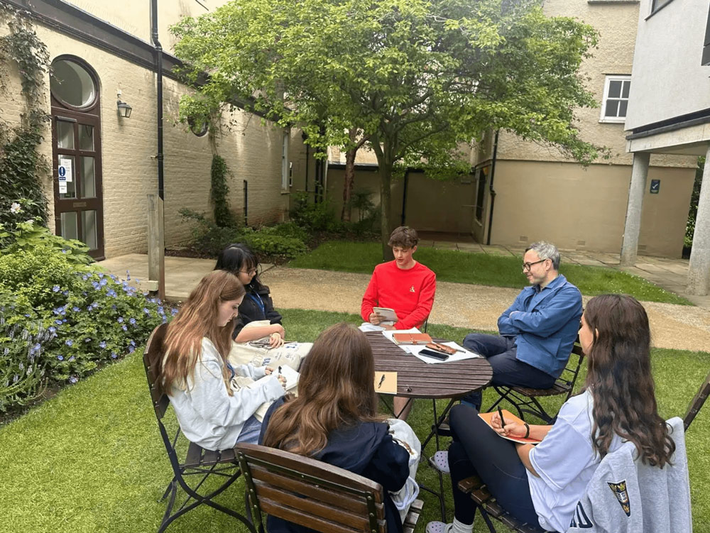 students and professor sit around a table outdoors