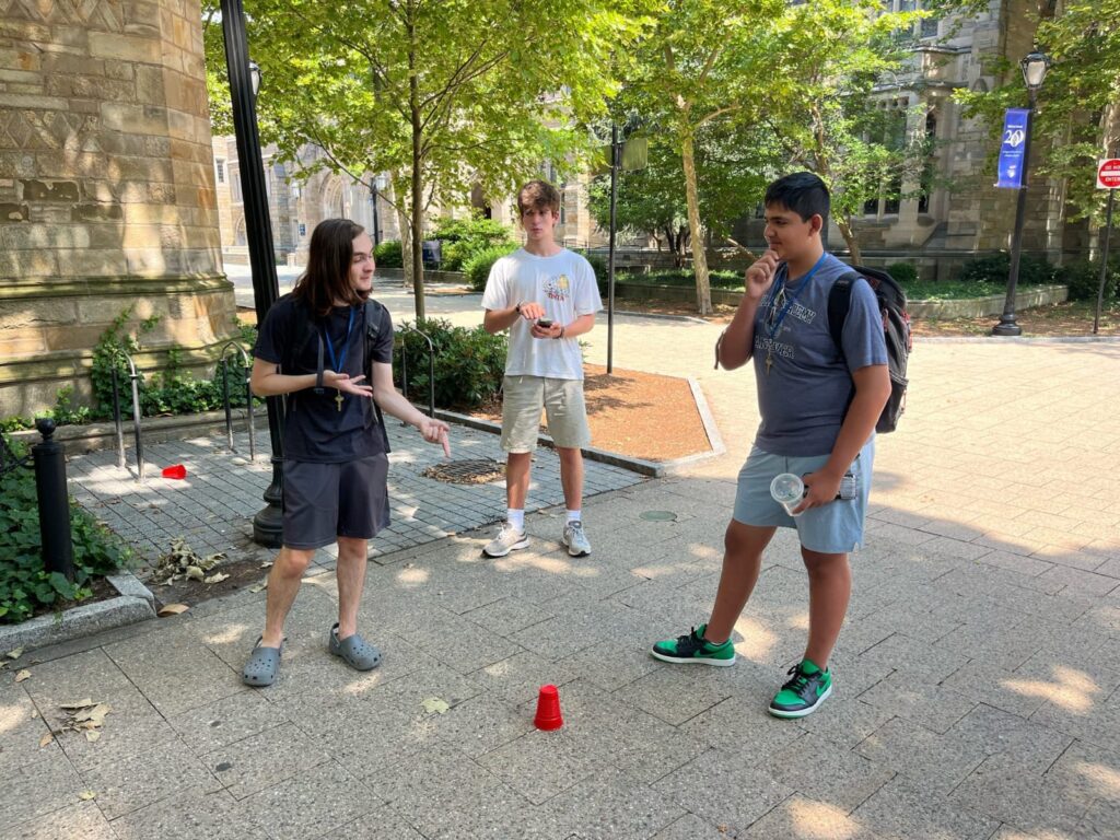 three students looking at a red cup on the ground