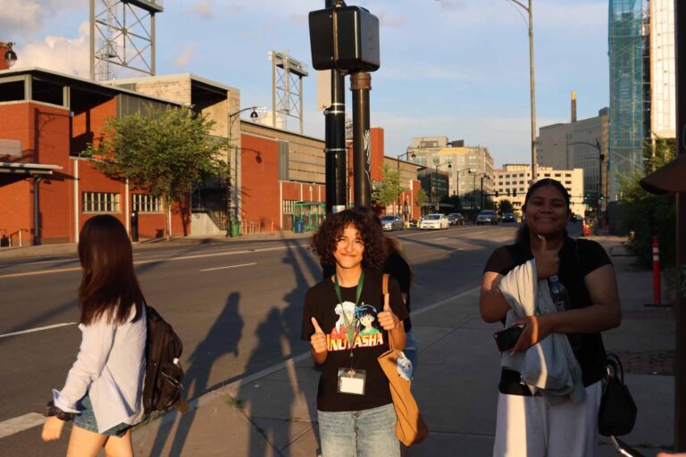 Three students guve thumbs up outside baseball stadium