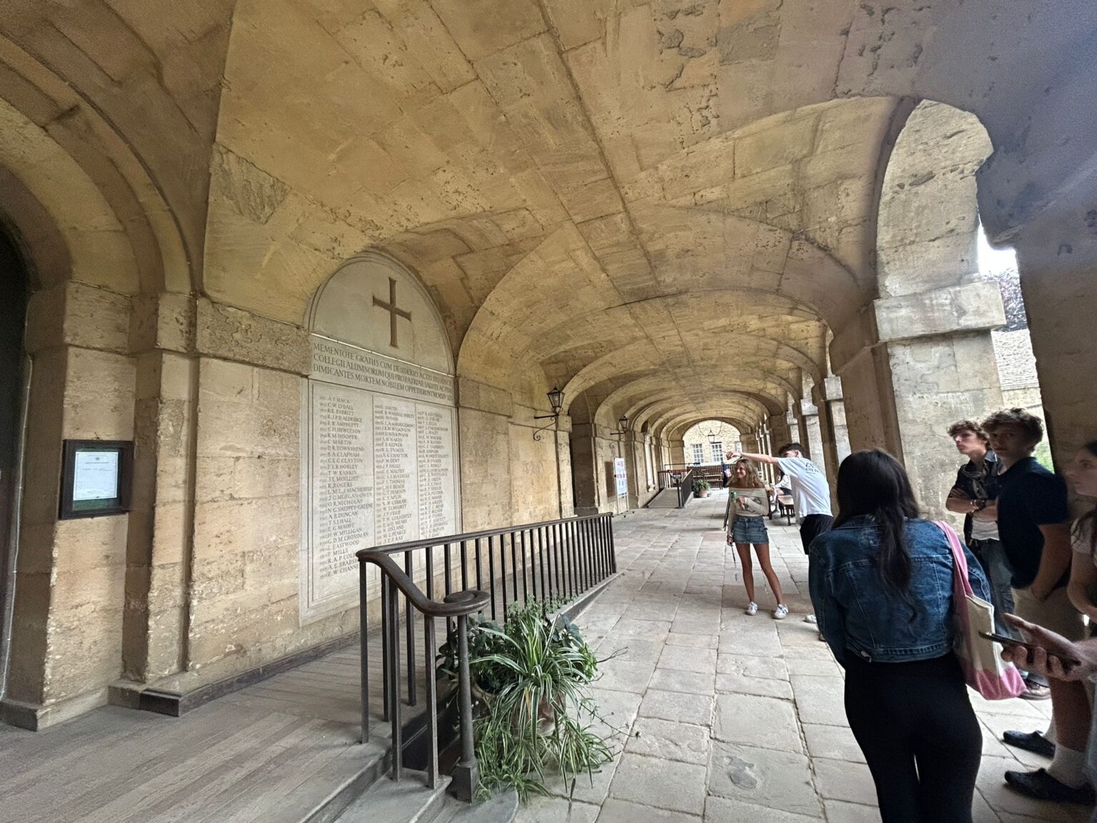 Instructor points at stone plaque with cross on a wall and students look on
