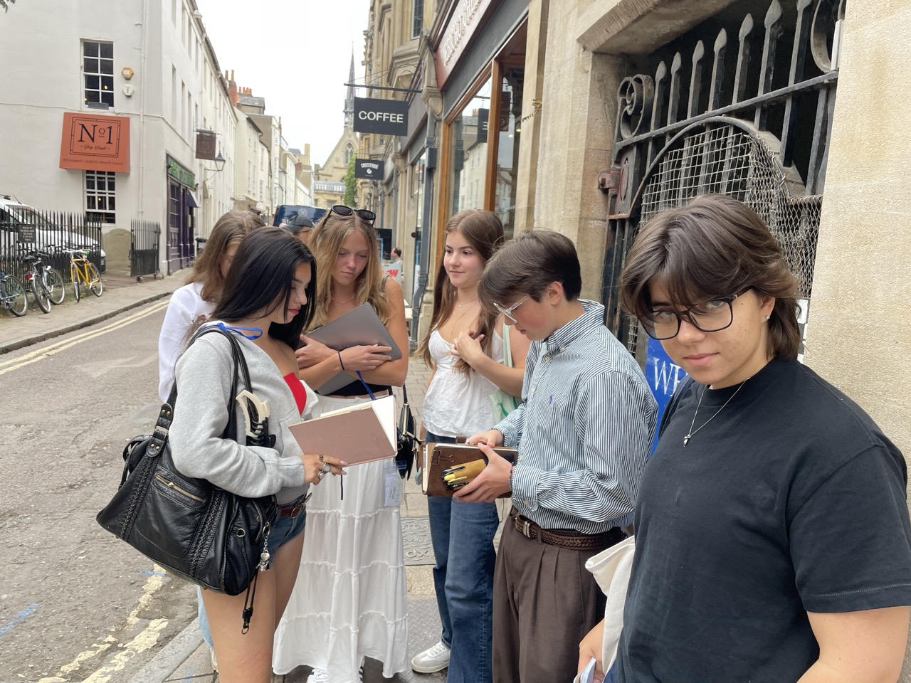 Group of students stand on street in Oxford writing in notebooks