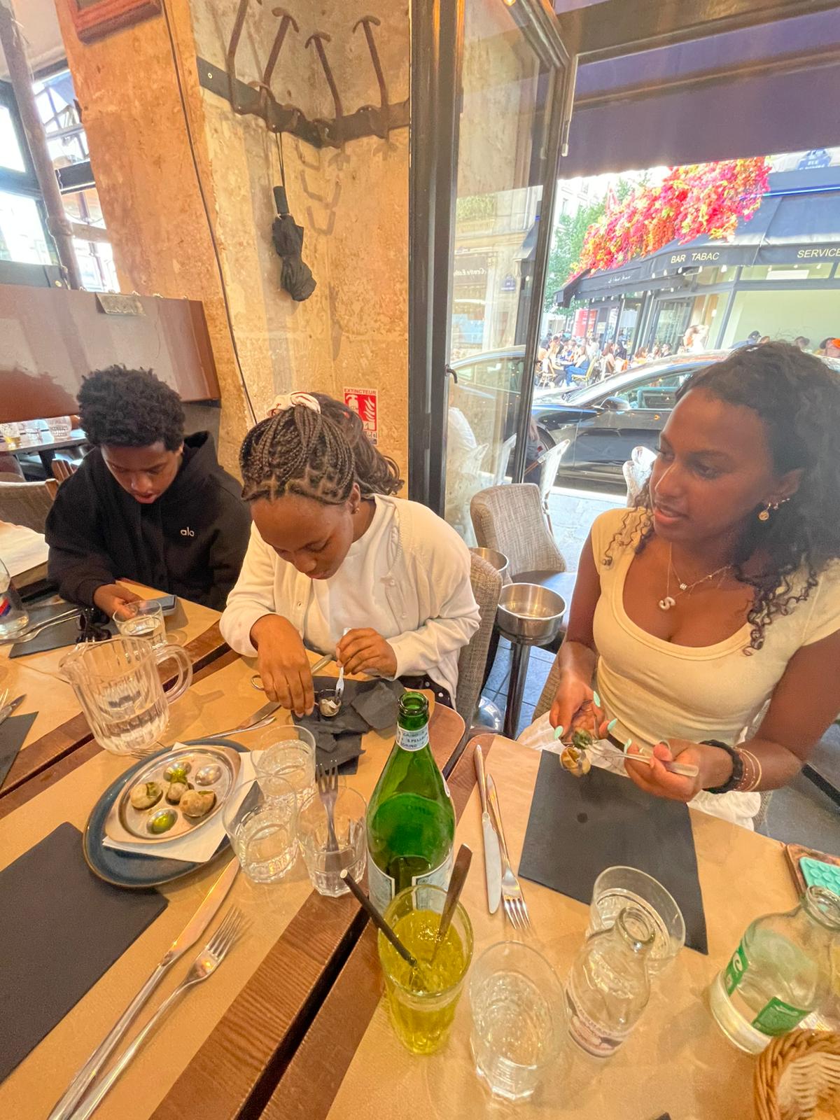Three student sitting at a dinner table poke at escargot