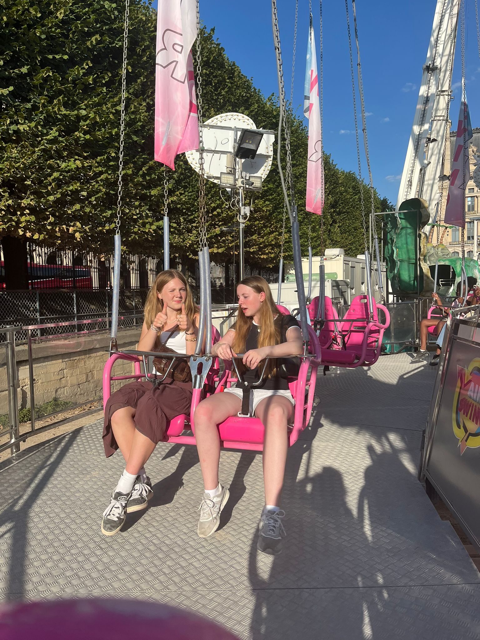 Two student sit on swings on carnival ride, one giving thumbs up to the camera