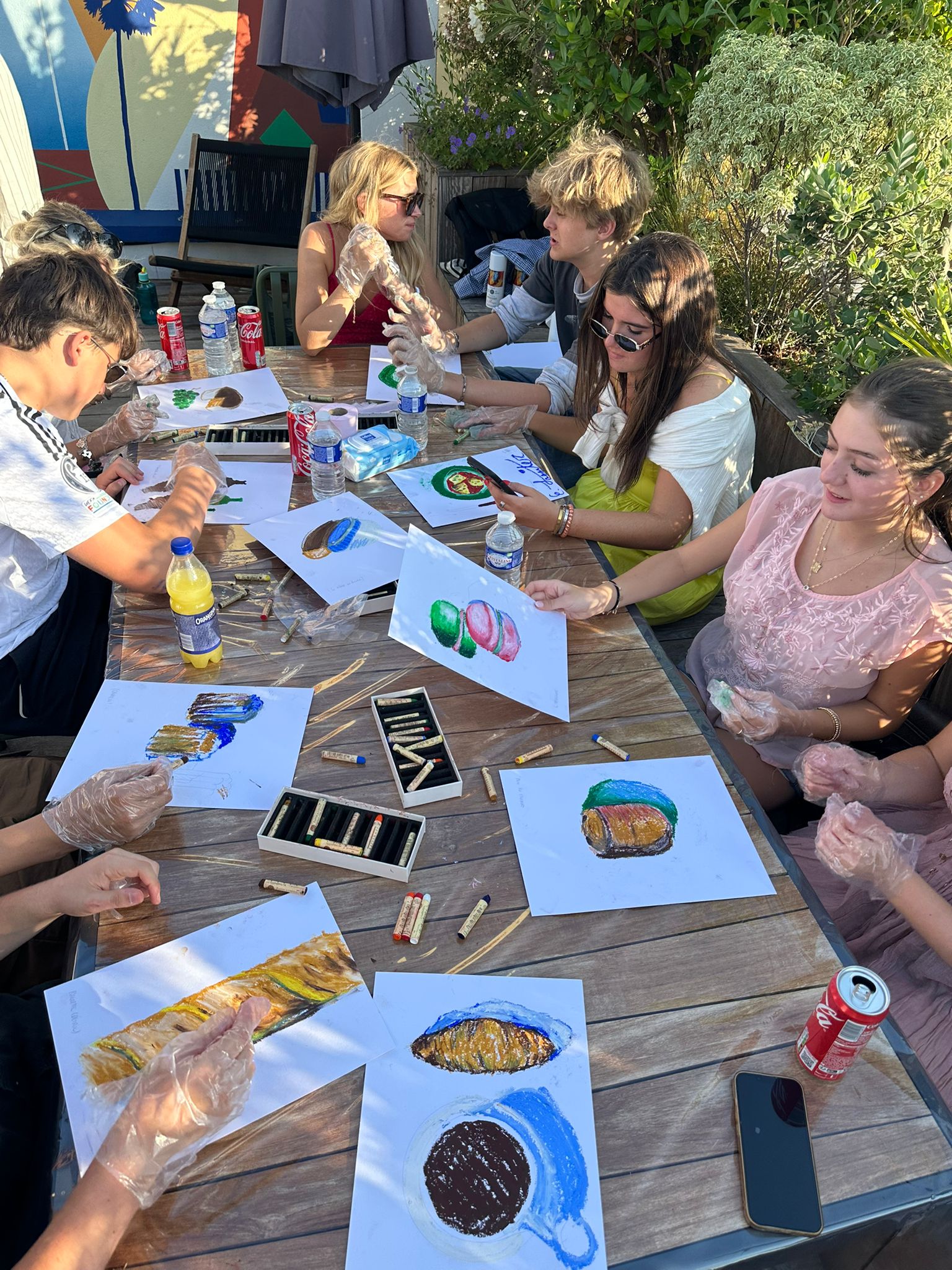 Group of student sit a table outside with finished oil pastel paintings