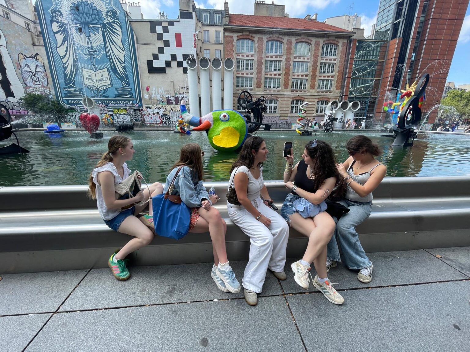 Group of students sit by foutain taking photo of it's modern art center piece