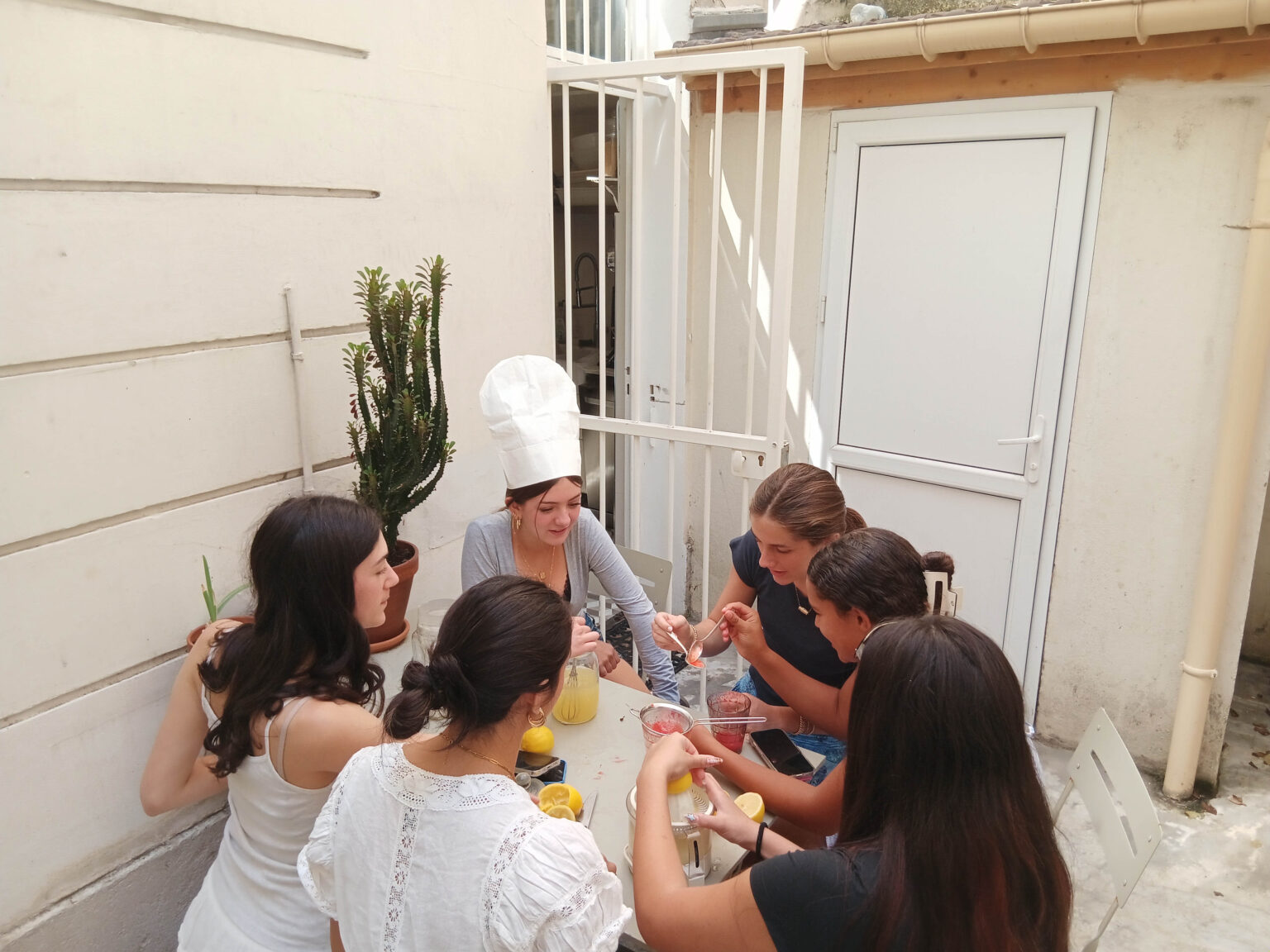 Group of students, one wearing a chefs hat, sit together cooking